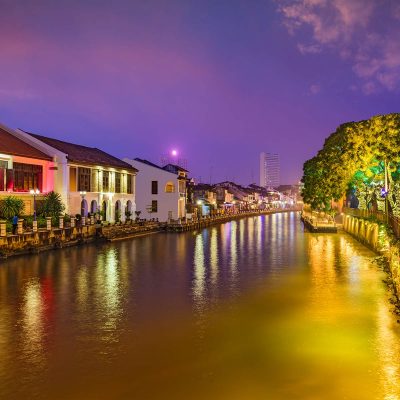 Scenic night view of Malacca River with colorful lights and heritage buildings, a popular stop on a Malacca tour from Kuala Lumpur.