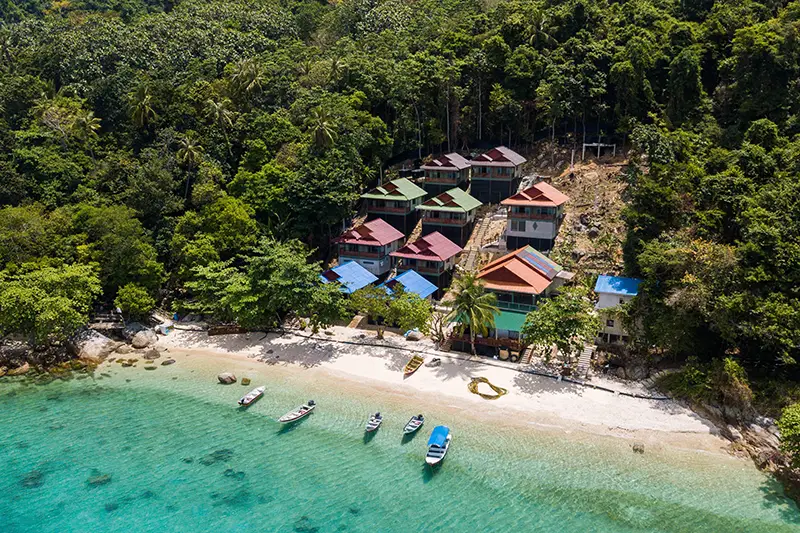 Aerial view of beachfront resorts surrounded by lush tropical forest and crystal-clear waters on Perhentian Island, a popular island in Malaysia.