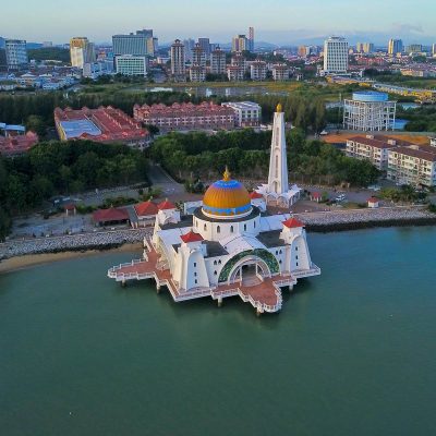 Aerial view of the Straits Mosque (Masjid Selat Melaka) built over the water in Malacca, Malaysia, with the city skyline in the background.