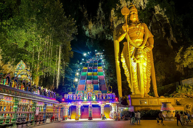 Batu Caves illuminated at night with its colorful staircase and golden Murugan statue, reflecting the long opening hours that allow tourists to visit flexibly.