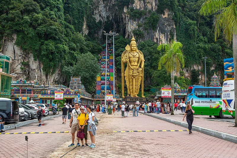 Tourists taking a photo in front of the giant Lord Murugan statue and rainbow staircase at Batu Caves during a Batu Caves tour in Malaysia