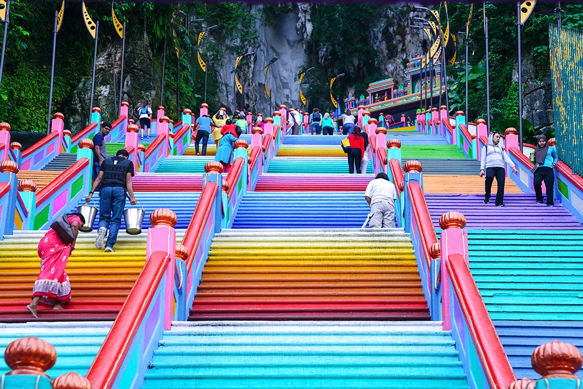 Visitors climbing the brightly painted 272-step rainbow staircase at Batu Caves during a Batu Caves tour in Malaysia