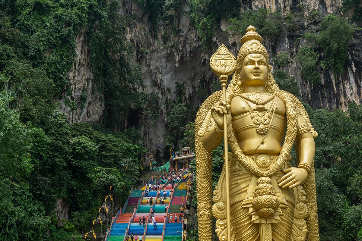 Golden statue of Lord Murugan and colorful staircase at Batu Caves temple in Malaysia, a highlight of any Batu Caves tour, surrounded by limestone cliffs and lush greenery