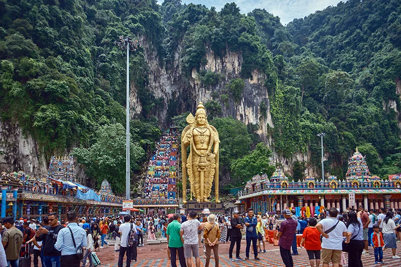 Crowd of tourists on a Batu Caves tour in Kuala Lumpur, with the giant Lord Murugan statue and colorful 272 steps leading to the Temple Cave.