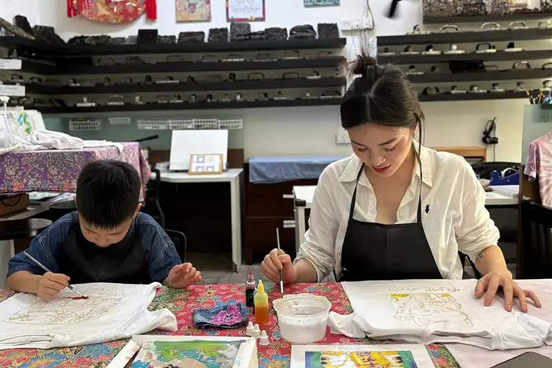 Tourist and child painting batik fabric during cultural workshop in Kuala Lumpur