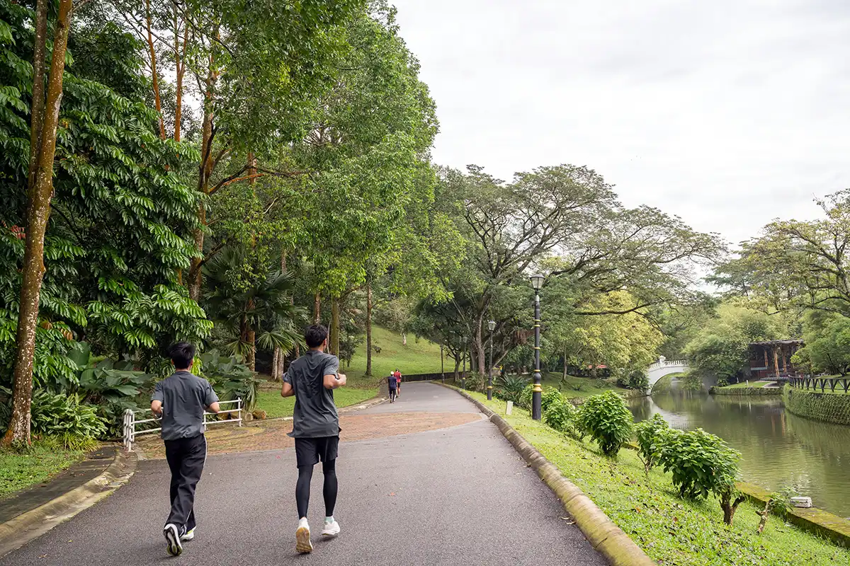 Jogging path at Perdana Botanical Garden in Kuala Lumpur, surrounded by trees, landscaped greenery and a calm lakeside area popular for outdoor activities.