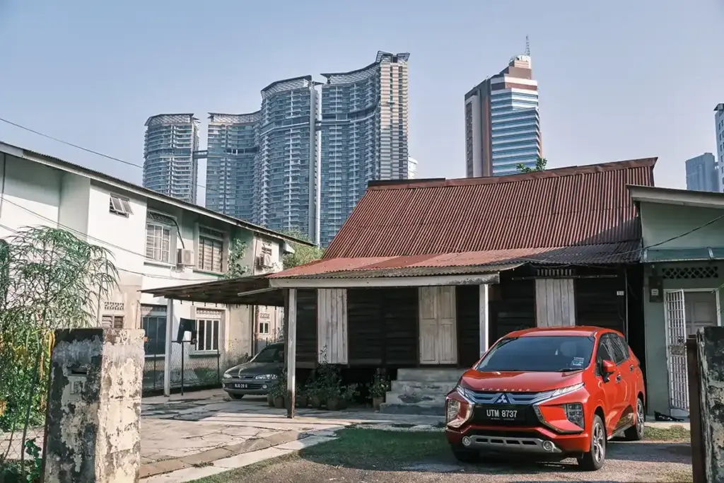 Traditional wooden Malay houses in Kampung Baru, Kuala Lumpur, with modern city skyscrapers in the background, showing the contrast between old neighbourhood life and the modern skyline.