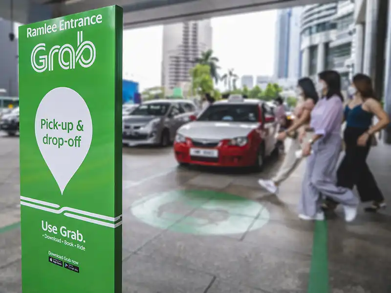 Grab pick-up and drop-off zone in Kuala Lumpur with tourists walking to e-hailing cars