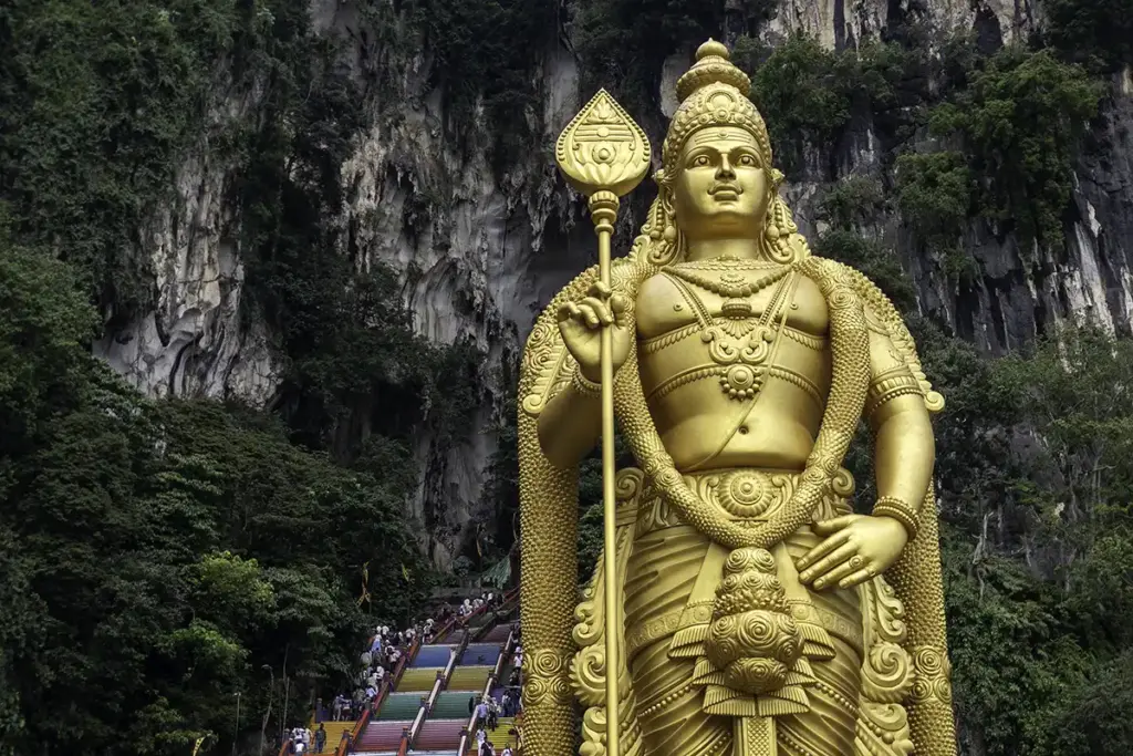 Golden Lord Murugan statue standing at the entrance of Batu Caves surrounded by limestone cliffs